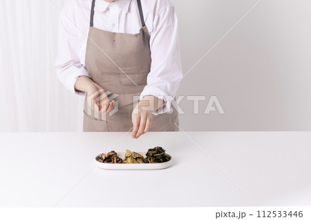 The woman is sprinkling sesame seeds with her hands on the finished vegetable dish The woman is sprinkling sesame seeds with her hands on the finished vegetable dish 112533446