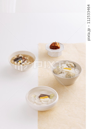 On a white table, three bowls of rice cake soup are placed with kimchi 112533464