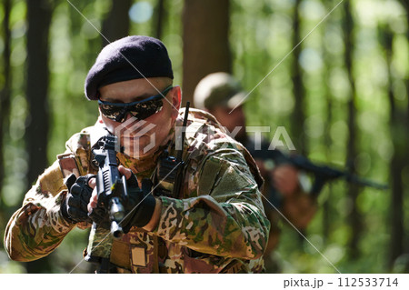 An elite soldier, camouflaged and stealthily navigating through dangerous woodland terrain, executes a covert mission in a secluded forest area An elite soldier, camouflaged and stealthily navigating through dangerous woodland terrain, executes a covert mission in a secluded forest area 112533714
