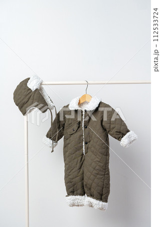 Baby gray quilted winter overalls on hanger against white wall 112533724