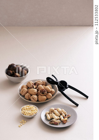 Chestnuts, walnuts, peanuts and pine nuts are served on each plate and there is a nutcracker next to it 112533802