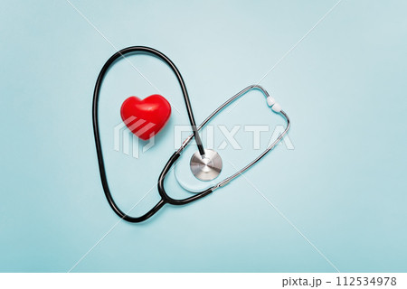 stethoscope with its tubing creating heart shape around red heart model on Pale Blue Background symbolizing love and care in the medical field. 112534978