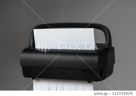 Black paper shredder cutting paper on gray background 112535024