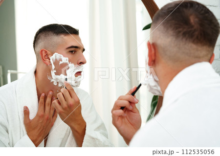 Reflection of a young man shaving in bathroom mirror close up 112535056