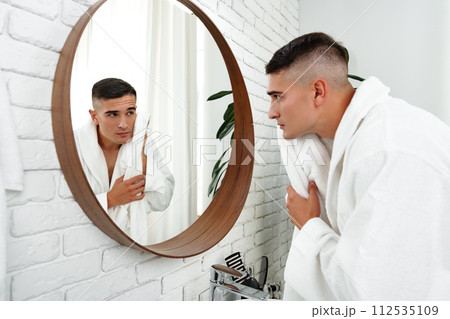 Young man looking in the mirror in the bathroom Young man looking in the mirror in the bathroom 112535109