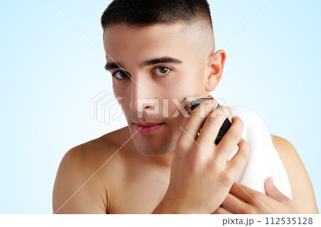 Handsome young man shaving face with electric razor on white background 112535128