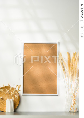 White blank photo frame with dry flowers in vase against white wall 112535414