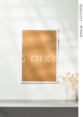 White blank photo frame with dry flowers in vase against white wall 112535650