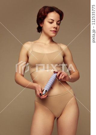 Tender young woman in cotton underwear holding vibrator against beige studio background. Intimacy and relaxation Tender young woman in cotton underwear holding vibrator against beige studio background. Intimacy and relaxation 112535775