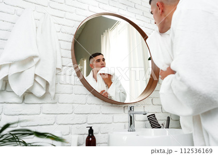 Young man looking in the mirror in the bathroom 112536169