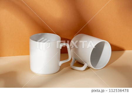 White ceramic mugs on peach background with shadows 112536478