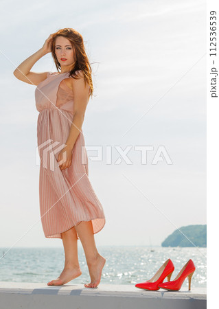 Woman wearing long light pink dress on jetty Woman wearing long light pink dress on jetty 112536539