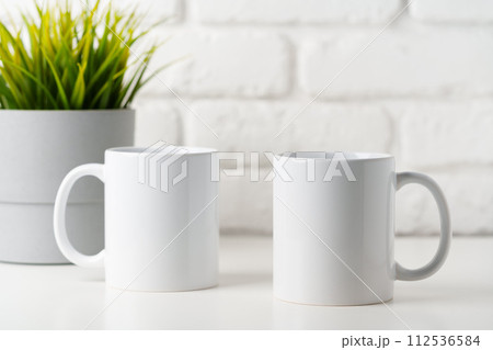 Two mugs on white table against brick wall background Two mugs on white table against brick wall background 112536584