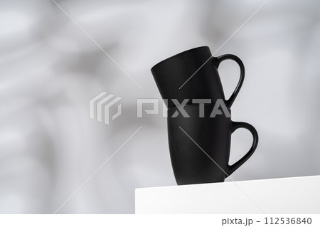 Two black ceramic mugs on gray background with shadows 112536840