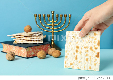 Matzo in hand, Torah, Hanukkiah and nuts on blue background Matzo in hand, Torah, Hanukkiah and nuts on blue background 112537044