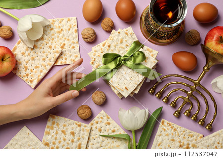 Matzo in hand, nuts, cup and flowers on pink background, top view Matzo in hand, nuts, cup and flowers on pink background, top view 112537047