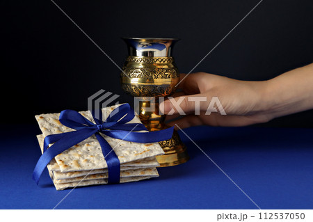 Matzo with ribbon and cup in hand on dark blue background 112537050