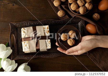Matzo, nuts, female hand, eggs and flower on tray on wooden background, top view 112537052
