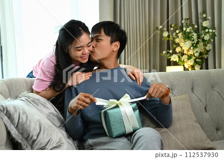 Happy young Asian man kissing cheerful girlfriend and thanking her for anniversary present 112537930