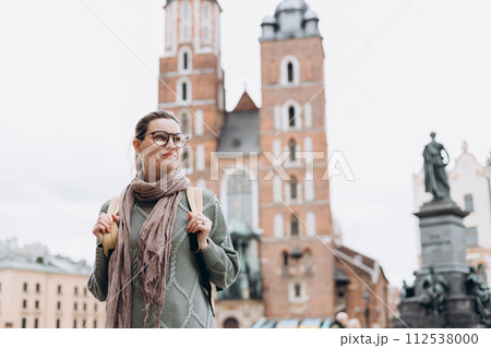 Tourist happy woman in glasses on Market Square in Krakow, Traveling Europe in autumn. St. Marys Basilica, cloudy day Tourist happy woman in glasses on Market Square in Krakow, Traveling Europe in autumn. St. Marys Basilica, cloudy day 112538000