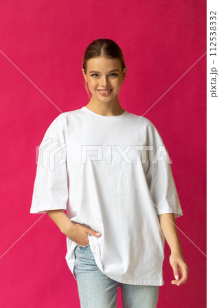 Beautiful blonde girl in a white oversized T-shirt and blue jeans posing on a gray background Beautiful blonde girl in a white oversized T-shirt and blue jeans posing on a gray background 112538332