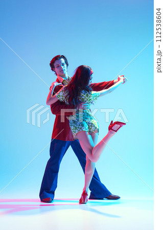 Artistic, talented, positive young man and woman, stylish couple dancing retro dance against blue background in neon light 112538604