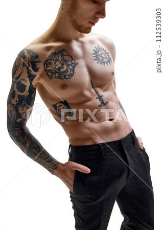 Close up of male model posing shirtless and demonstrating his muscular body in tattoos against white studio background. Copy space. Close up of male model posing shirtless and demonstrating his muscular body in tattoos against white studio background. Copy space. 112539303