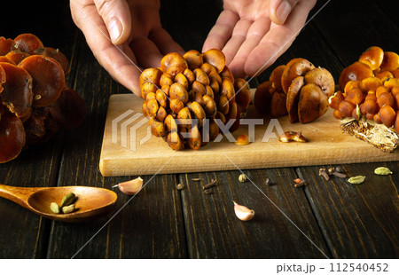 Close-up of a chef hands sorting raw fresh Flammulina velutipes or velvet shank mushrooms on a kitchen board before preparing a diet dinner 112540452