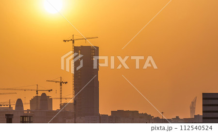 A tower in Doha timelapse, Qatar, under construction, silhouetted against the sunset. 112540524