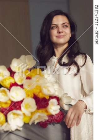 Beautiful woman with spring flowers tulips in hands sitting on chair near window. Women's Day 112541282