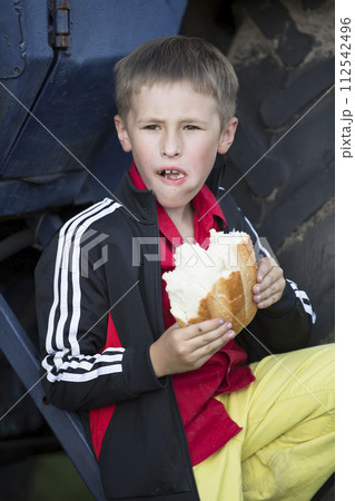 A funny little boy is hungry and is eating a big bun. 112542496