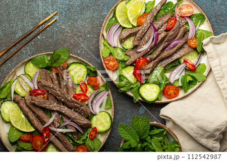 Two plates with traditional Thai beef salad with vegetables and mint top view served on rustic concrete background, healthy exotic asian meal 112542987