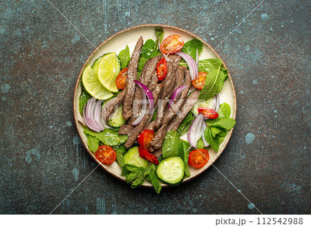 Plate with traditional Thai beef salad with vegetables and mint top view served on rustic concrete stone background, healthy exotic asian meal 112542988