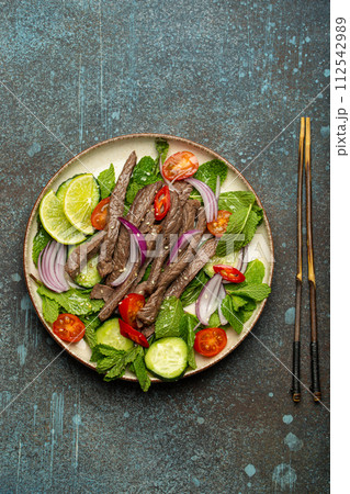 Plate with traditional Thai beef salad with vegetables and mint top view served on rustic concrete stone background, healthy exotic asian meal 112542989