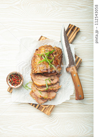 Rolled turkey roasted with spices and herbs on baking paper with knife and wooden white background top view. Baked cut for slices turkey fillet roll for dinner 112543058