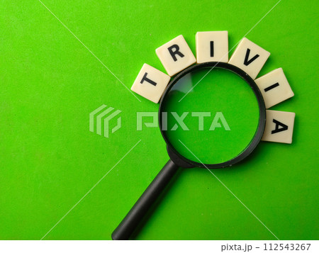Top view magnifying glass and word toys with text TRIVIA on a green background. Top view magnifying glass and word toys with text TRIVIA on a green background. 112543267