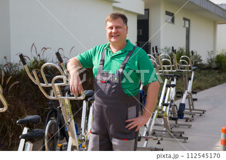 Male mechanic tidying up bicycles and exercise equipment for vacationers Male mechanic tidying up bicycles and exercise equipment for vacationers 112545170