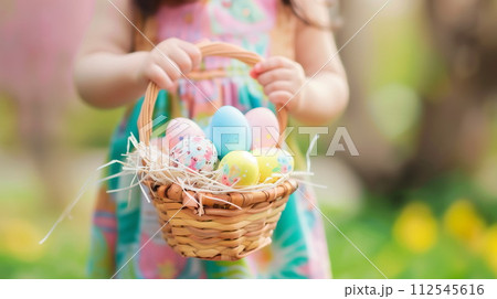 Little child wearing pastel color dress holding basket with easter eggs in spring garden. Generative AI 112545616