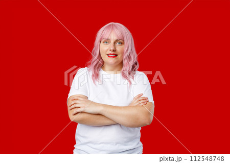 Excited happy 30s woman with pink hair standing on red background in studio. Crossed arms. 112548748