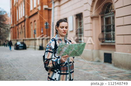 Happy cheerful young woman with map walking on city street, Urban lifestyle concept. Traveler. Attractive female tourist with backpack is exploring new city. 112548749