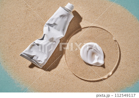 A tube of moisturizing sunscreen and a smear on a sandy background. A tube of moisturizing sunscreen and a smear on a sandy background. 112549117