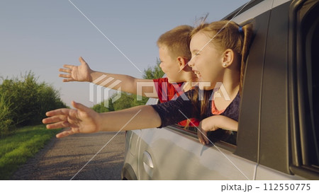 happy children boy girl leaning out car window waving arms, happy faces child kid schoolchildren. girl older sister, with smile face, cheerfully leads wind hand, brother laughs next sister. joyful happy children boy girl leaning out car window waving arms, happy faces child kid schoolchildren. girl older sister, with smile face, cheerfully leads wind hand, brother laughs next sister. joyful 112550775