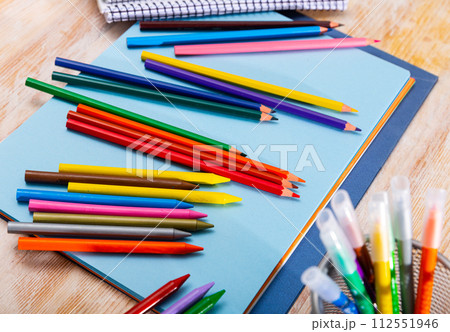 Multicolored pencils and papers on wooden background 112551946