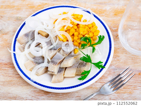 Slices of spicy marinated herring fillet with corn and onion 112552062