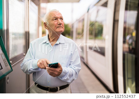 Old man with smartphone on tram stop 112552437
