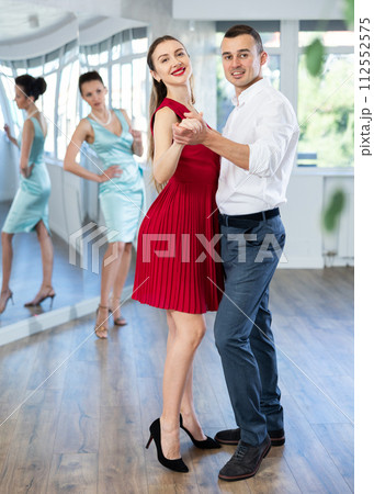Woman in red learning to dance waltz with man in studio Woman in red learning to dance waltz with man in studio 112552575
