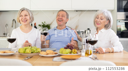Happy pensioners gathered at festive table - talking, discussing news and drinking red wine 112553286