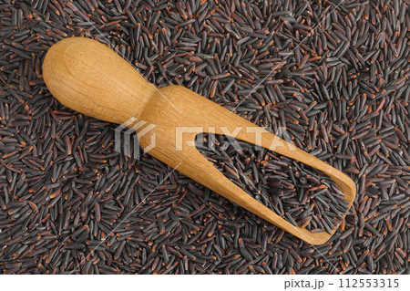 Black rice in a wooden scoop as a background. Top view. Flat lay 112553315