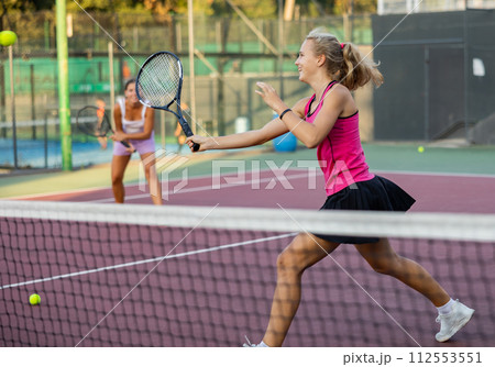 Sporty teenager girl player hitting ball with racket during friendly doubles couple match Sporty teenager girl player hitting ball with racket during friendly doubles couple match 112553551