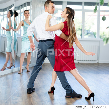Couple in stage costumes learns tango dancing during individual lesson 112553554